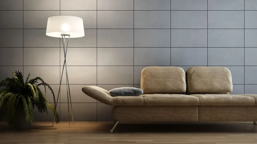 Modernes Wohnzimmer Interieur mit beigem Sofa, Stehlampe mit weißem Schirm und grüner Zimmerpflanze vor einer grauen Wand mit quadratischen Fliesen. Gemütliche Atmosphäre.