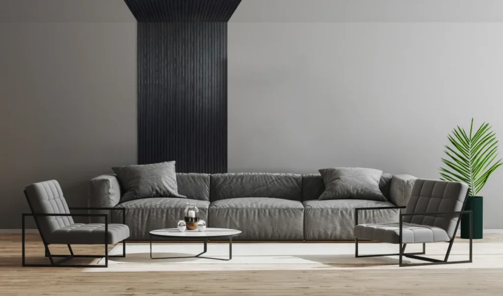 Modernes Wohnzimmer mit grauem OLMO Sofa, zwei Sesseln, Couchtisch und einer schwarzen Wandgestaltung. Zimmerpflanze sorgt für einen Farbakzent.