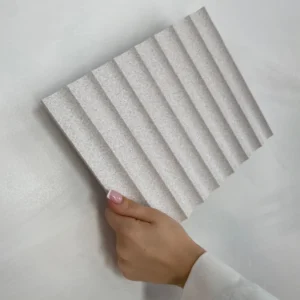 Nahaufnahme einer Hand, die eine strukturierte Gresso Natural Light Platte hält. Die Platte zeigt ein wellenförmiges Design und eine helle, natürliche Farbgebung. Ideal für Wandgestaltung und Innendesign.